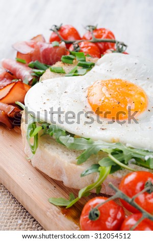 Big breakfast with egg, tomato, bacon and rocket on toast served on rustic wooden board. heart conscious