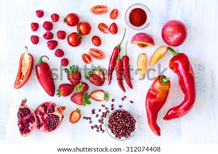 Collection of fresh red toned vegetables and fruits raw produce on white rustic background, peppers capsicum chilli strawberry raspberry pomegranate tomato paprika azuki beans plum