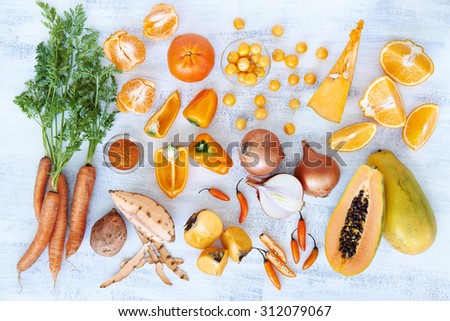 Selection of assorted fresh orange toned vegetables and fruit raw produce on white rustic background, pumpkin butternut carrot papaya pawpaw capsicum pepper sweet potato cherry tomatoes chilli orange