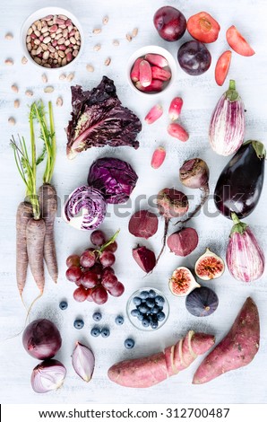 Collection of fresh purple toned vegetables and fruits on white rustic background, eggplant, beetroot, carrot, fig, plum, aubergine, cabbage, grapes, radishes, loose leaf lettuce