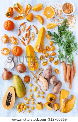 Collection of fresh orange toned vegetables and fruit raw produce on white rustic background, pumpkin butternut carrot papaya pawpaw capsicum pepper sweet potato cherry tomatoes chilli orange