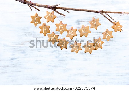 Gingerbread stars with \'merry christmas\' tied with bakers twine, hanging off a bare branch on white rustic background