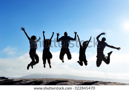 Silhouettes of group of friends jumping outdoors on a beach in unison with arms up