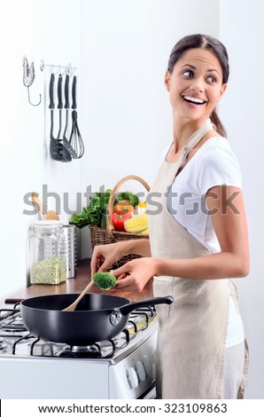 Woman standing by the stove in the kitchen, looking over her shoulder while she stirs and cook
