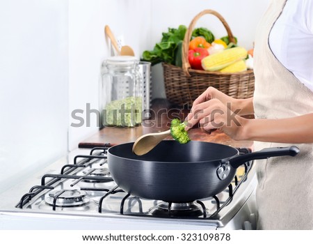 Domestic scene of anonymous woman cooking by the gas stove adding some broccoli