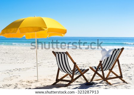 Beach chairs and yellow umbrella in sand with bright sunlight