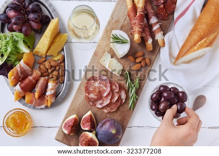 Hands getting an olive, cured meat charcuterie selection salami, chorizo, prosciutto wrapped bread sticks with fresh fig, rock melon, almonds and white wine