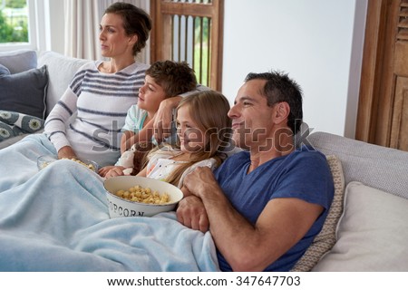 Happy Caucasian family with two children relaxing at home, kids brother and sister watching a movie and having popcorn with parents