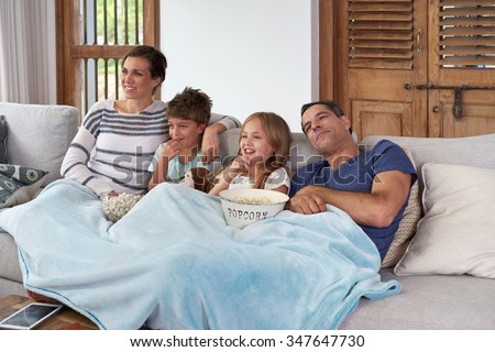 Happy laughing Caucasian family with two children relaxing at home, kids brother and sister watching a movie and having popcorn with parents