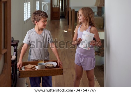Smiling caucasian brother and sister siblings carrying surprise mothers day breakfast tray
