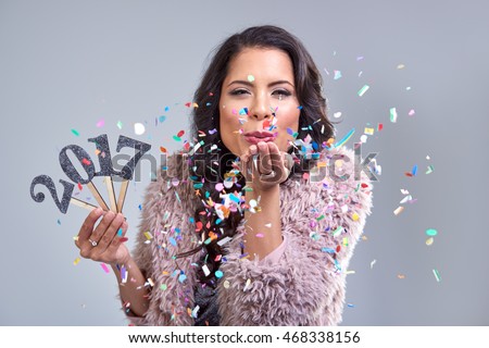 Pretty glamourous woman welcoming the new year 2017 blowing confetti into camera, photobooth style image