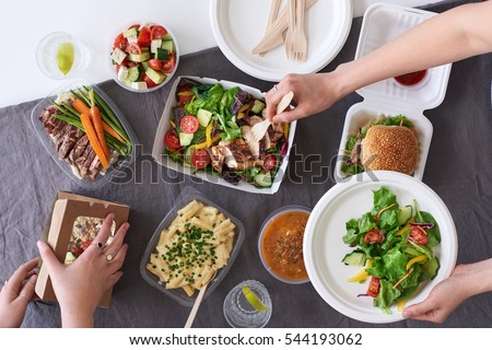 Convenient takeaway takeout food for party, overhead spread of assorted food with hands serving up