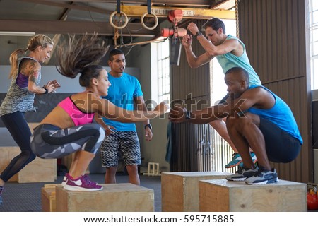 Instructor giving encouragement while fit strong healthy people do box jumps in crossfit gym
