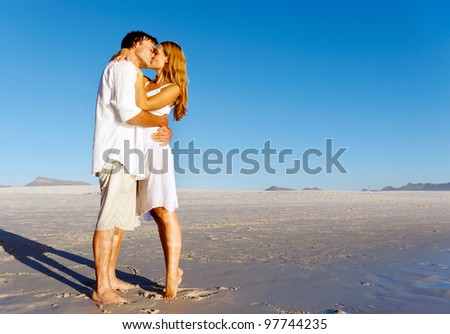 Couple in love stand on the beach in summer and share a kiss at sunset alone and on honeymoon.