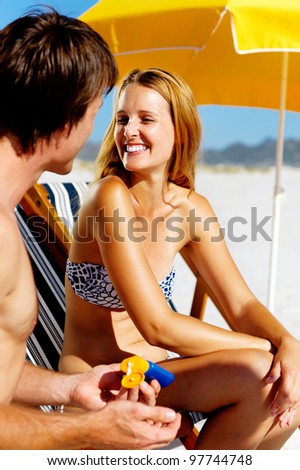 Summer beach couple take care of their skin with sunblock lotion of high SPF for maximum protection