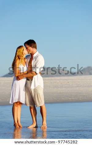 Couple in love stand on the beach in summer and share a kiss at sunset alone and on honeymoon.