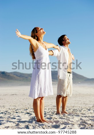 Young stress free couple enjoy the summer sun on the beach. Arms out, heads back and carefree attitudes.
