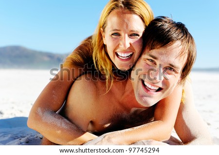 affectionate young couple enjoy a summer beach vacation and throw sand all over each others faces.