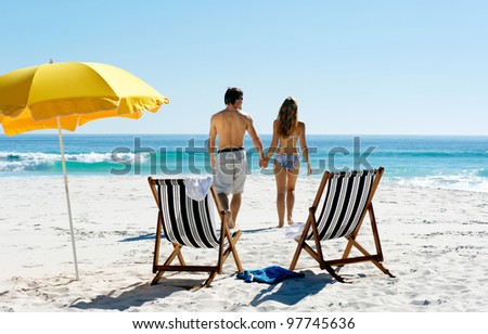 Tropical summer beach holiday couple walk towards the ocean holding hands while on honeymoon vacation