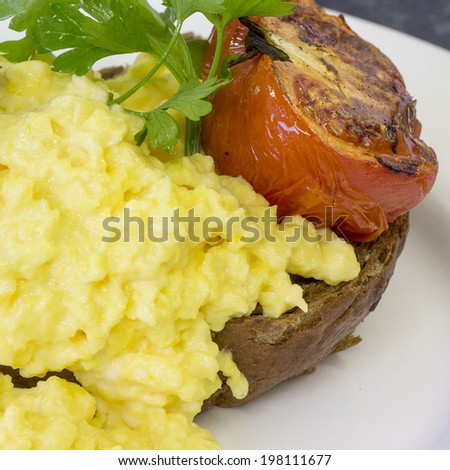 Scrambled eggs on brown toast with grilled tomato