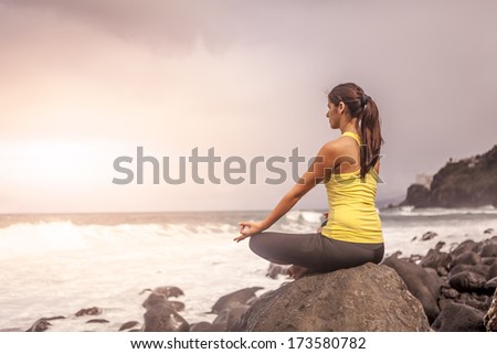 young woman practicing yoga meditation on the beach at sunset, lotus position