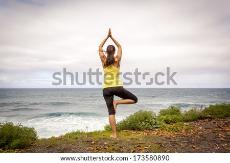 Young woman practicing tree yoga pose near the ocean