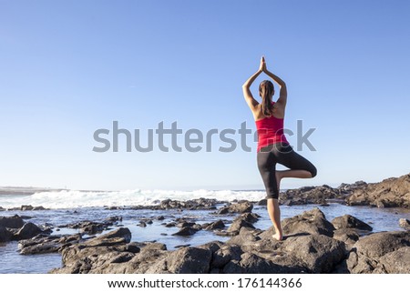 Young woman practicing tree yoga pose near the ocean