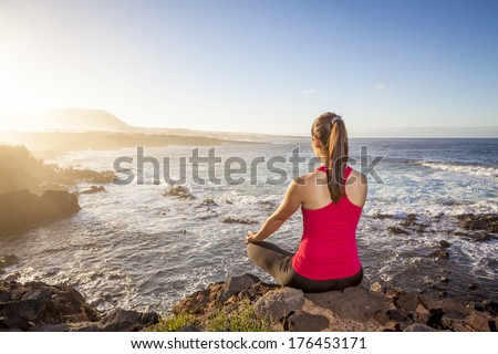 young woman practicing yoga meditation on the beach at sunset