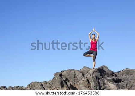 Young woman practicing tree yoga pose outdoor against blue sky