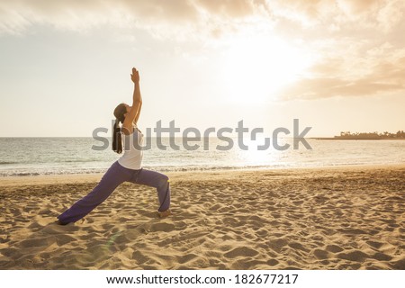 Young woman practicing yoga warrior pose on the beach near the ocean at sunset