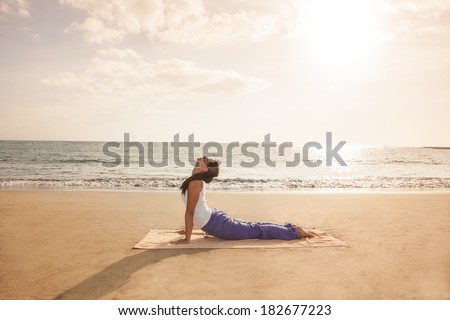 Young woman practicing yoga cobra pose on the beach near the ocean at sunset