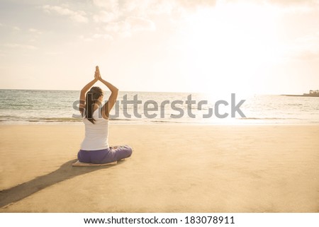 young woman practicing yoga meditation on the beach at sunset