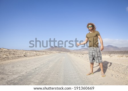 Travel man hitchhiking. attractive young man hitchhiker by the road during trip in the desert