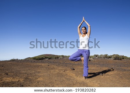 Young woman practicing tree yoga pose outdoor on a desert mountain