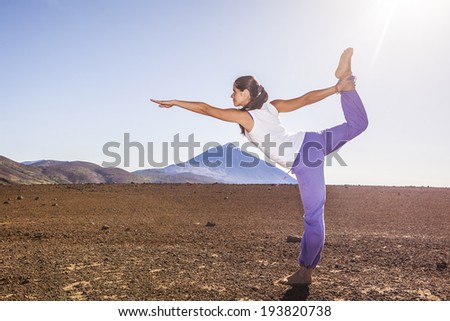 Young attractive woman doing dancers yoga pose outdoors on a desert mountain