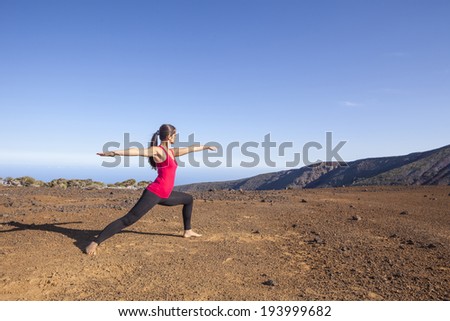 Young woman practicing yoga warrior pose on a desert mountain