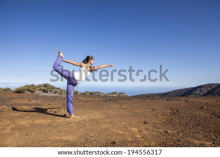 Young attractive woman doing dancers yoga pose outdoors on a desert mountain