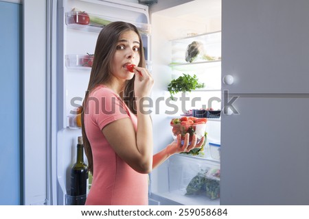 young beautiful woman eating strawberries from the fridge. Healthy Eating Concept.