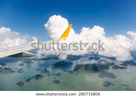 Wing of the plane with blue sky and cloud over island sea