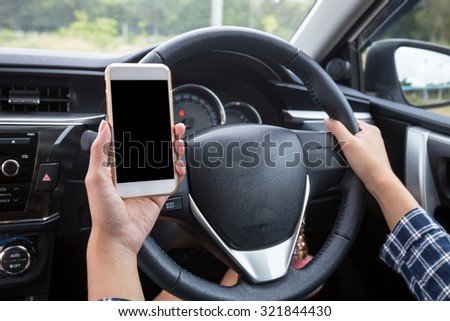 Young female driver using touch screen smartphone and hand holding steering wheel in a car.