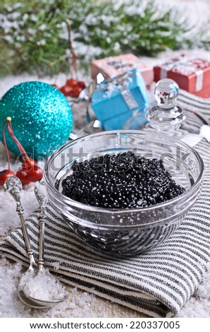 Fish caviar black in a glass is a special container on striped napkin on the background of fir branches, snow and New Year gifts