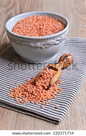Small red lentils in a wooden scoop is on the bright striped napkin
