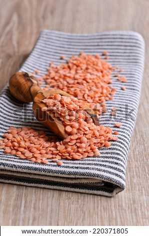 Small red lentils in a wooden scoop is on the bright striped napkin