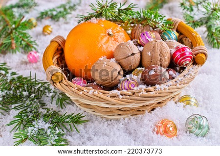 Walnuts and hazelnuts are in a wicker basket on the background of white snow, fir branches and bright balls