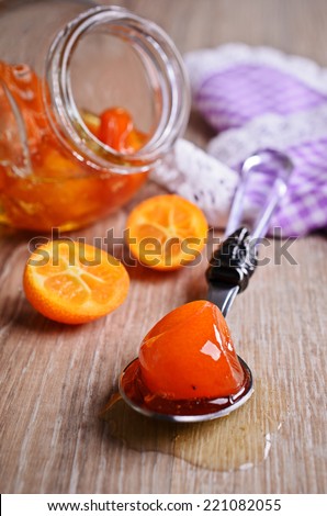 Jam from the whole kumquats lies in the spoon against the background of the glass jar