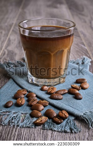 Glass of dark liquid on the background of whole coffee beans