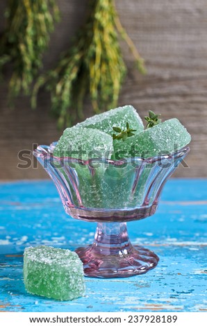 Jelly candy green color in the glass vase on the background of thyme leaves