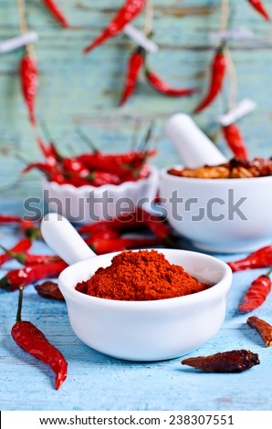 Powder red chilly pepper in a white ceramic bowl on the background of dry pods and old wooden boards