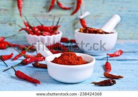 Powder red chilly pepper in a white ceramic bowl on the background of dry pods and old wooden boards
