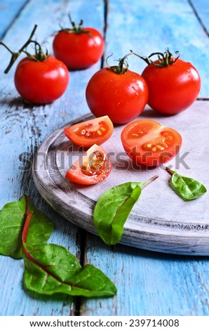 Fresh red tomatoes whole and in the context of the old painted wood surface against the green salad leaves